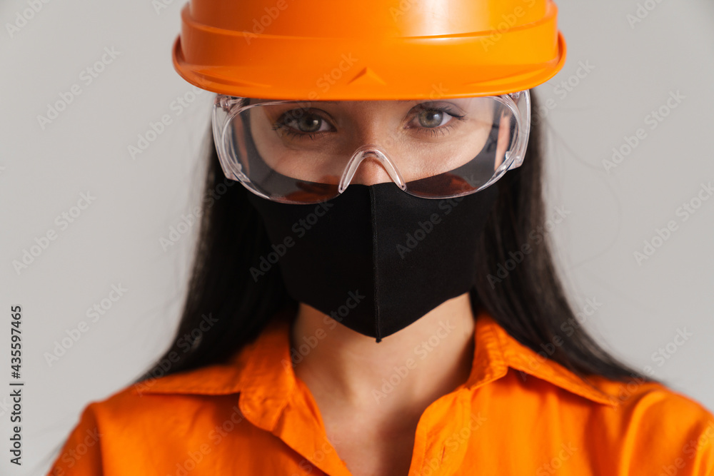 Young brunette woman in safety glasses and face mask looking at camera Young brunette woman in safety glasses and face mask looking at camera