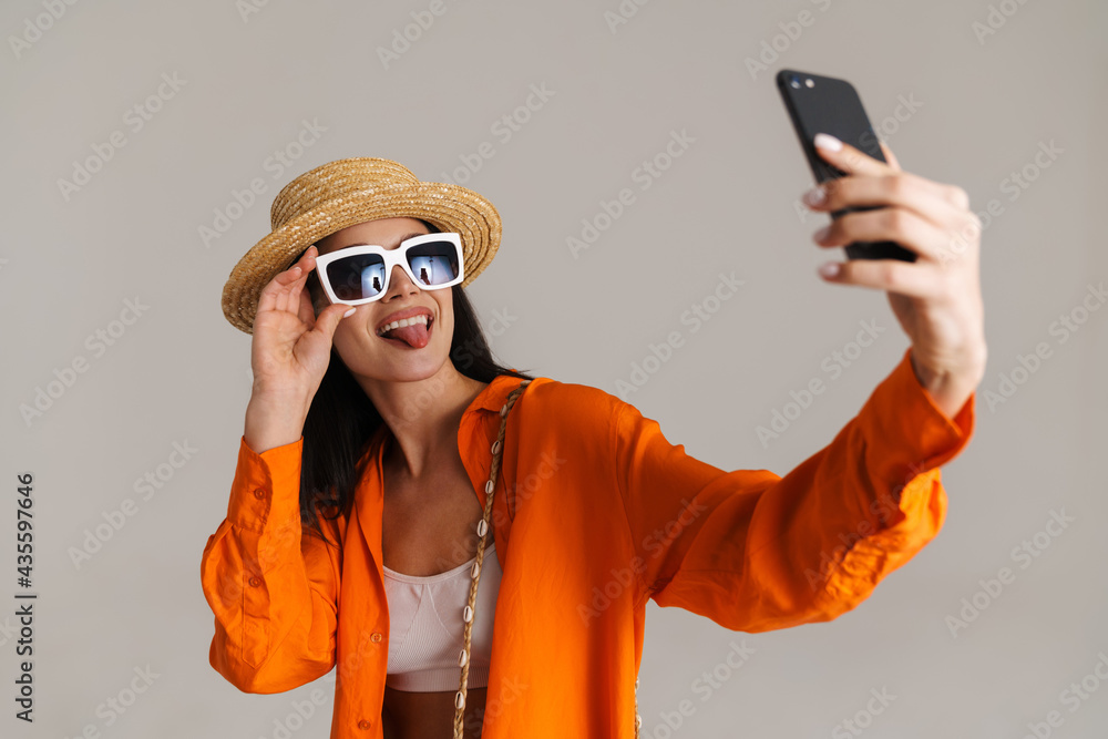 Young brunette woman in hat and sunglasses smiling at camera Young brunette woman in hat and sunglasses smiling at camera