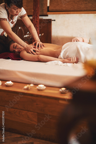 Masseuse pressing pair of massage stones to woman left shoulder