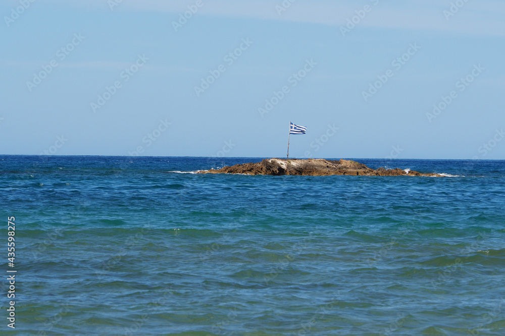 Flaga Grecji na małej kamienistej wyspie przy brzegu, Kreta Flaga Grecji na małej kamienistej wyspie przy brzegu, Kreta