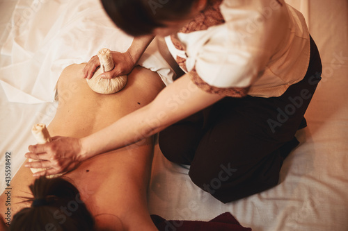 Massagist putting herbal compress balls on upper and lower back