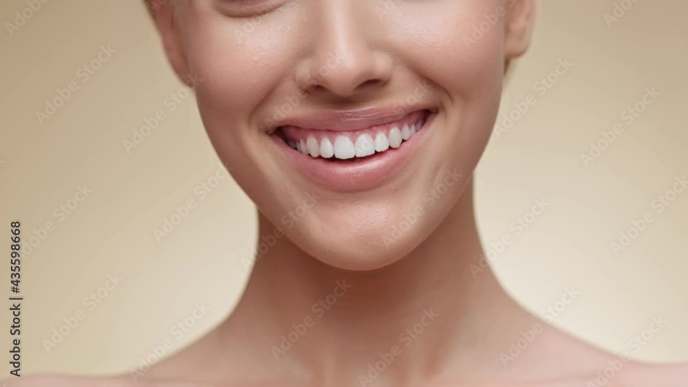 Closeup of woman smiling to camera, showing white smile of after teeth alignment procedure, beige background Closeup of woman smiling to camera, showing white smile of after teeth alignment procedure, beige background