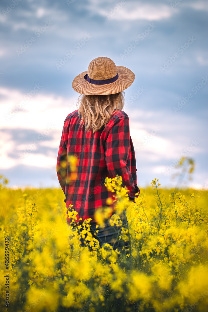 Woman farmer standing in blooming rapeseed field and looking at sky