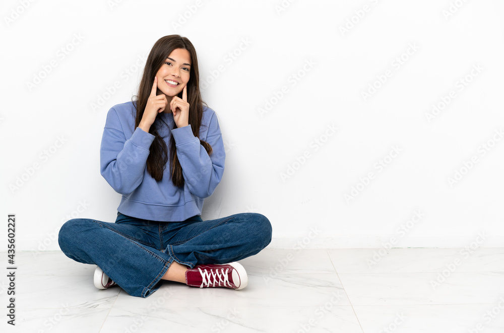 Young woman sitting on the floor smiling with a happy and pleasant expression Young woman sitting on the floor smiling with a happy and pleasant expression
