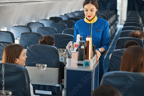 Cabin attendant leading trolley cart through plane aisle