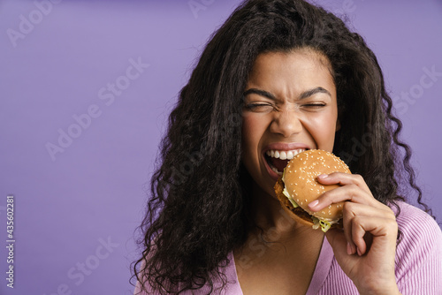 Young black woman with curly hair laughing while eating hamburger