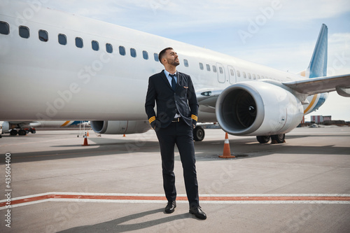 Pilot looking far away while standing on runway near plane
