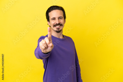 Young caucasian man isolated on yellow background showing and lifting a finger