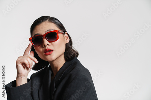 Brunette asian woman wearing jacket and sunglasses looking at camera
