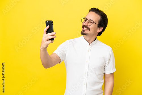 Young caucasian man isolated on yellow background making a selfie © luismolinero