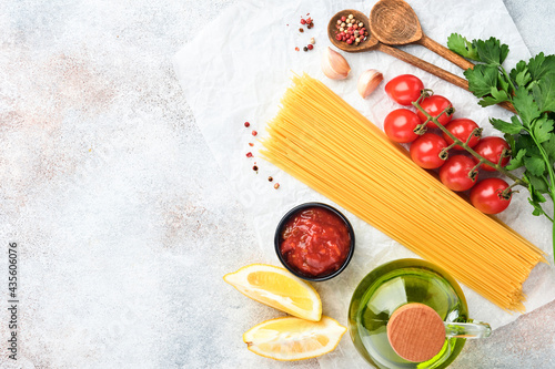 Pasta background. Pasta spaghetti, tomato ketchup sauce, olive oil, spices, parsley, and fresh tomatoes on a light grey slate table. Food cooking background. Top view with copy space.