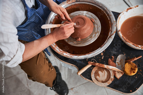 Pottery master forming the back of clay bowl with instrument photo