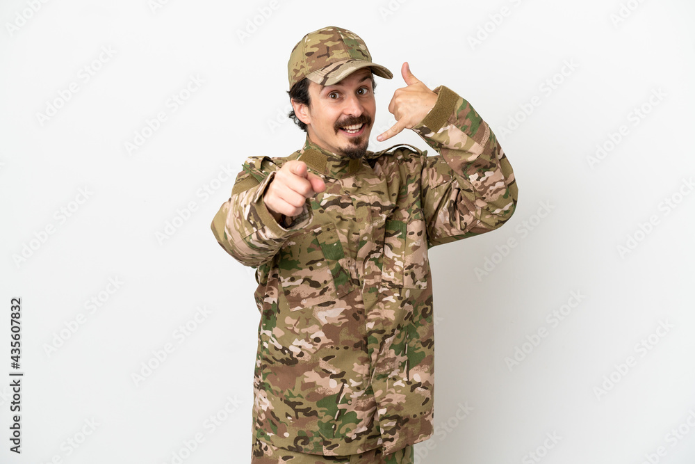 Soldier man isolated on white background making phone gesture and pointing front Soldier man isolated on white background making phone gesture and pointing front