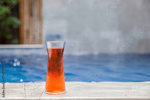 Cool tea in a glass bottle placed at the edge of the swimming pool in the house