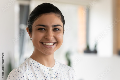 Head shot portrait of confident successful smiling Indian businesswoman standing in office, happy entrepreneur employee executive looking at camera, posing for corporate photo, profile picture