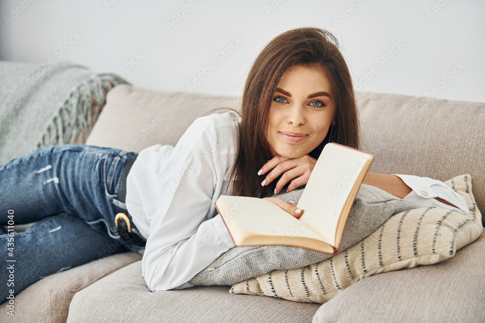 With book. Beautiful young woman in jeans and white shirt is at home With book. Beautiful young woman in jeans and white shirt is at home