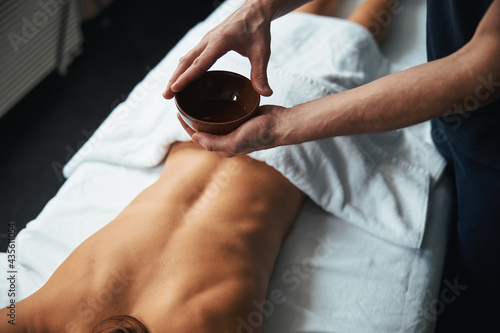 Focused image of male masseur holding bowl with cosmetic butter in beauty center