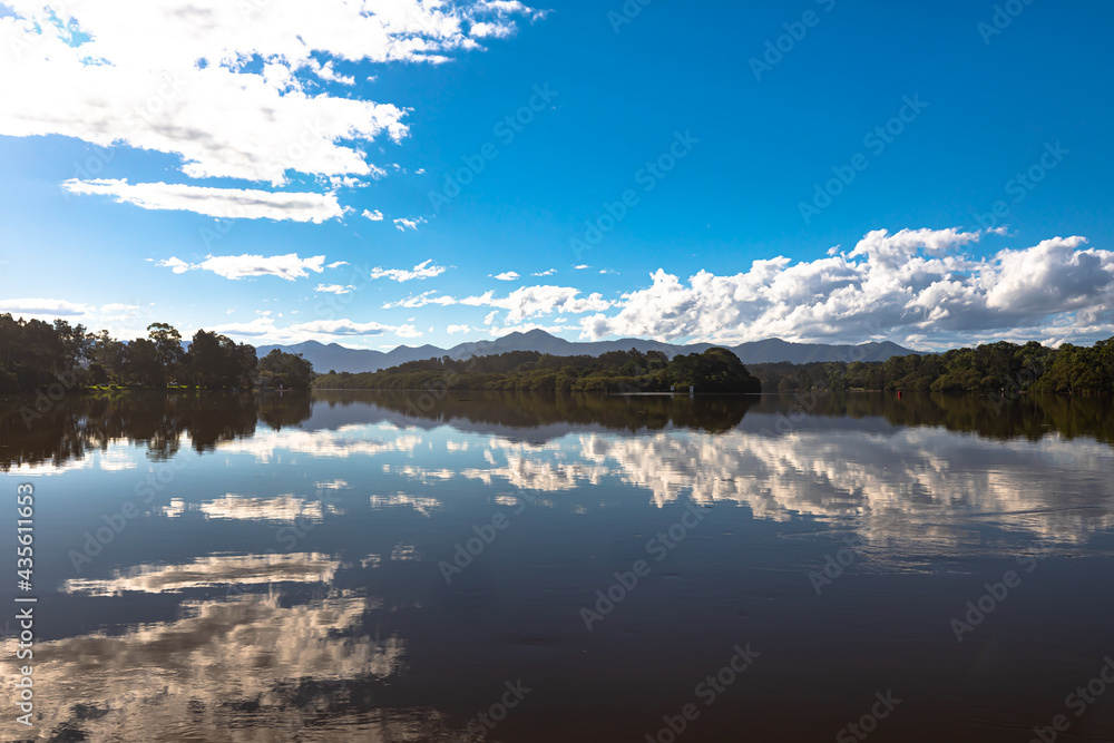Panorama of calm lake, river on blue sky with clouds reflected in the water at Bellinger River, Australia.