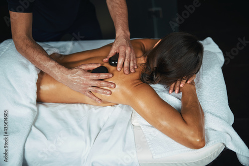 Peaceful charming female lying on massage table while receiving professional manual procedure in wellness health center
