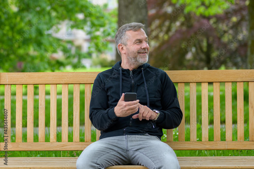 Fototapeta premium Happy relaxed middle-aged man using his mobile in a park