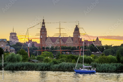 blue masted boat sailing along the river along the park