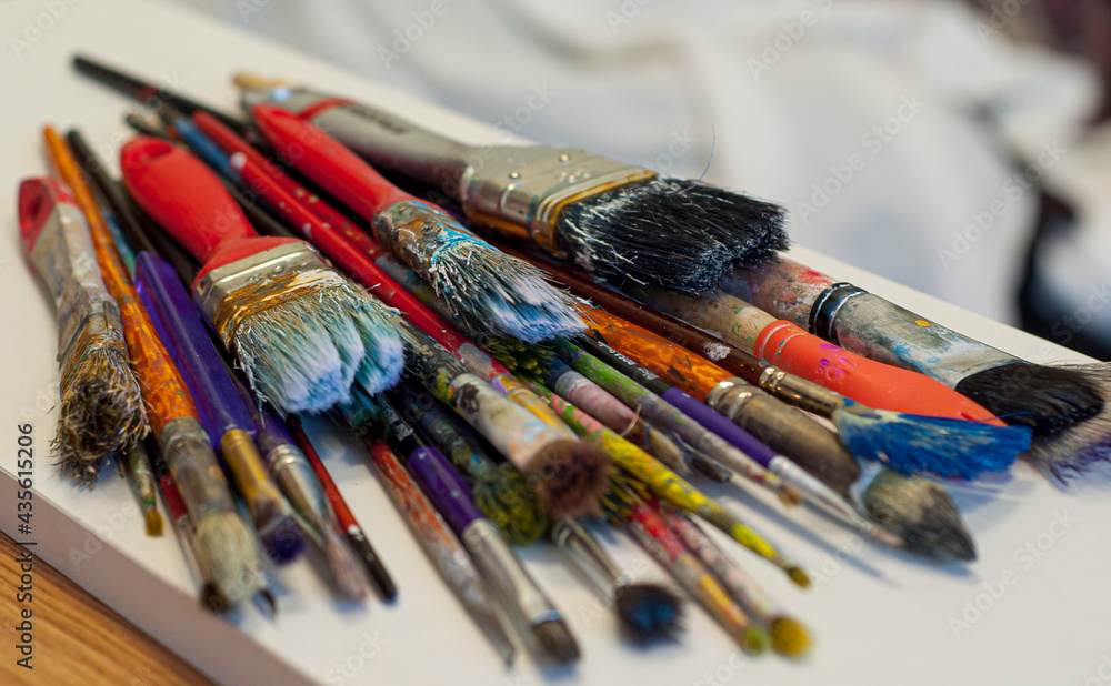 Obraz premium dirty brush set on the table. brushes with colorful paints displayed side by side. paint brushes with gouache on white
