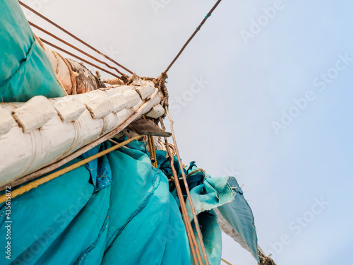 A fragment of a white wooden mast and a turquoise sail of a felucca boat. Bottom view, against the background of the sky. photo