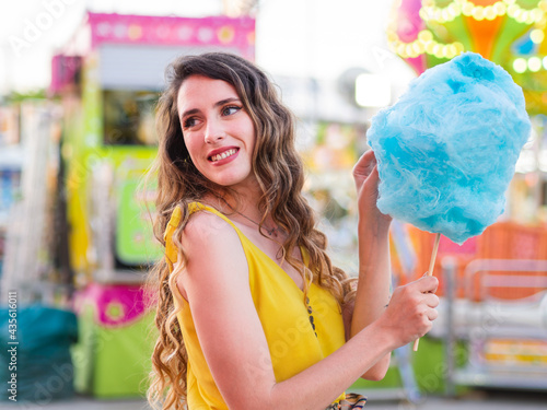 Mujer joven disfrutando de un algodón de azúcar en la feria o parque de atracciones