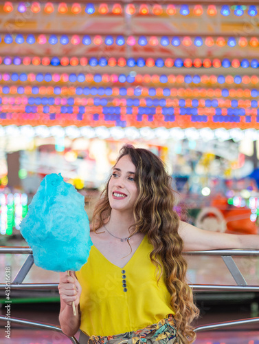 Mujer joven disfrutando de un algodón de azúcar en la feria o parque de atracciones
