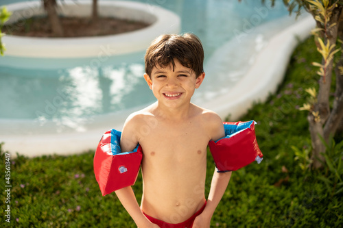 Boy with muffs looking at camera in his garden pool