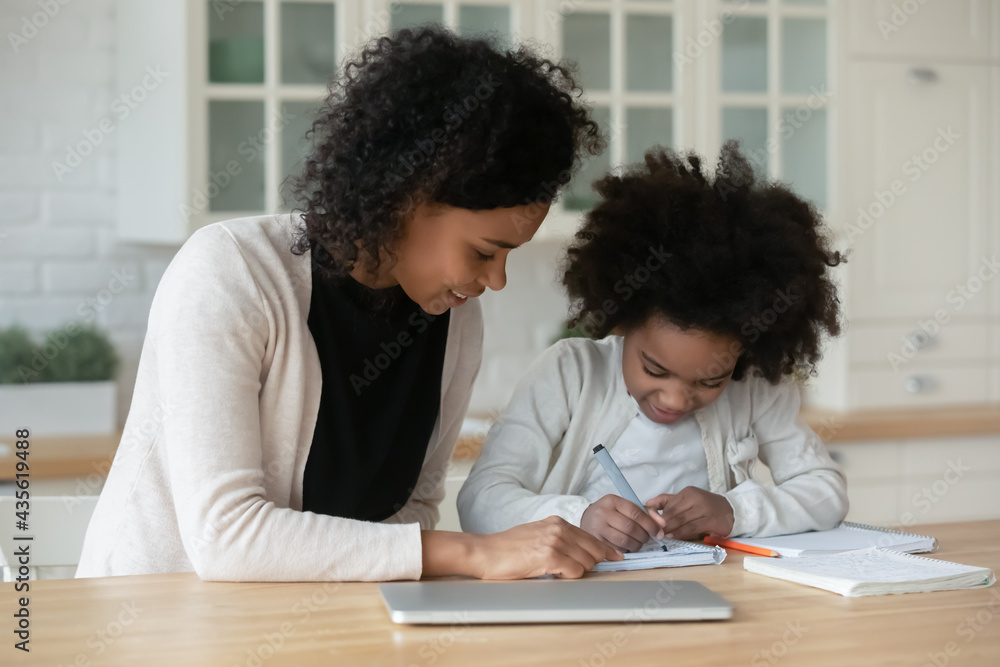 Happy young biracial mother help little schoolgirl with preparation for school learning together at home. Smiling caring African American mom and small daughter study write. Education concept. Happy young biracial mother help little schoolgirl with preparation for school learning together at home. Smiling caring African American mom and small daughter study write. Education concept.