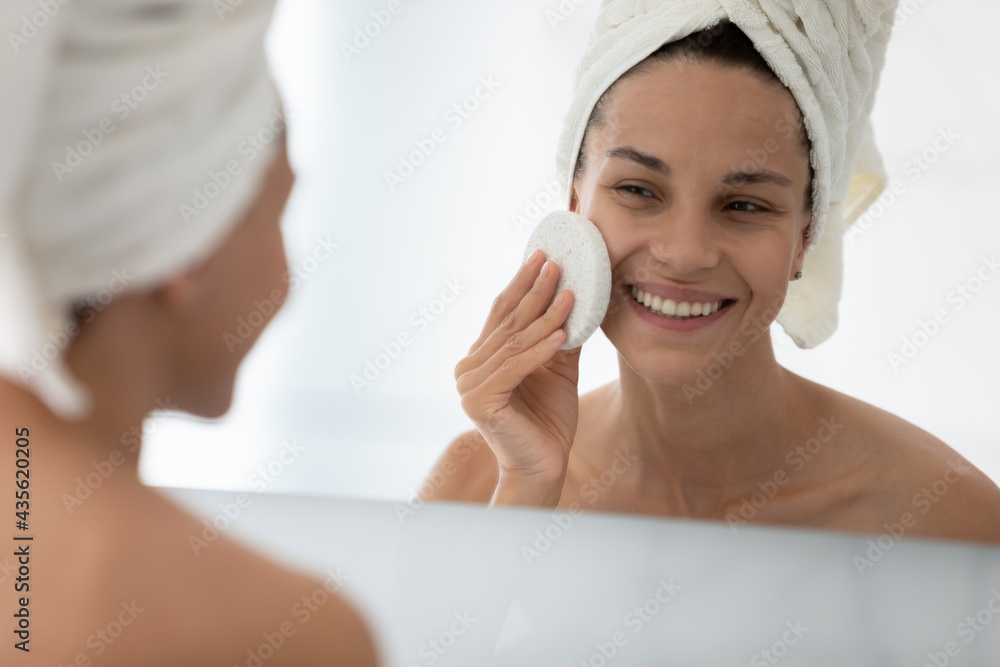 Happy beautiful girl cleansing facial skin with skincare exfoliating sponge, washing face with cleanser, lotion for pure pores after shower. Home cosmetic procedures, acne treatment concept Happy beautiful girl cleansing facial skin with skincare exfoliating sponge, washing face with cleanser, lotion for pure pores after shower. Home cosmetic procedures, acne treatment concept