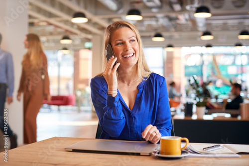 Young Businesswoman Sitting At Desk On Phone Call In Modern Open Plan Office