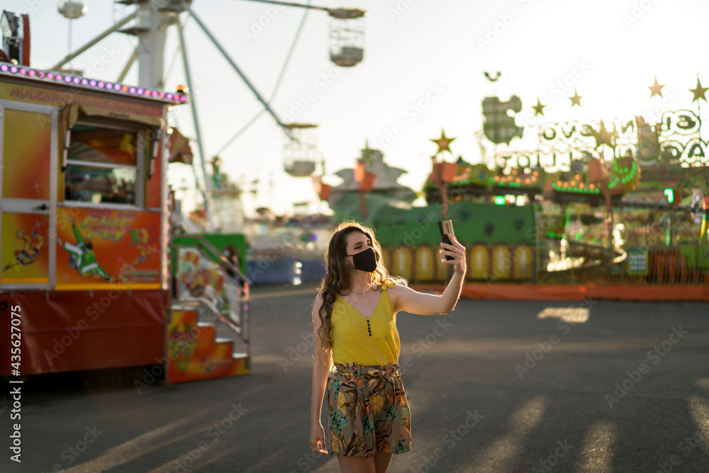 Mujer joven positiva en vestido de verano haciendo selfie y divirtiéndose en el parque de atracciones