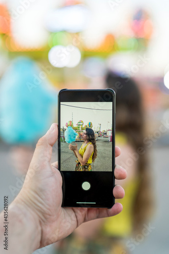 Mujer joven atractiva en vestido de verano haciendo un selfie en el parque de atracciones visto a través de la cámara del smarpthone