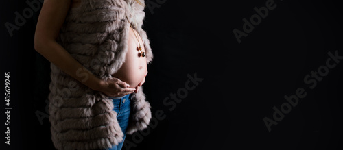 Tablou pe pânză Belly of pregnancy women, hand holding tummy and expecting baby and mexican bola or chiming pendant, harmony ball, angel caller