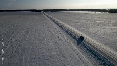 Aerial clip of white SUV driving down a snowy straight road in rural North Dakota in the winter.  photo