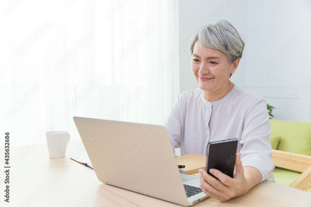 Senior Asia woman is working from home, using laptop and smart phone. Senior Asia woman is working from home, using laptop and smart phone.