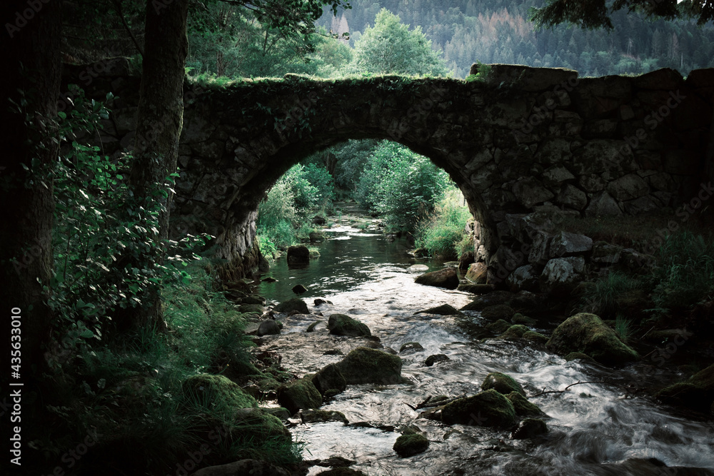 Dark ancient medieval stone bridge on a mountain river stream