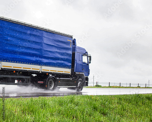 A blue semi-trailer truck drives on a wet highway during the rain in summer. The concept of poor visibility and traffic hazards on the road. Copy space for text photo