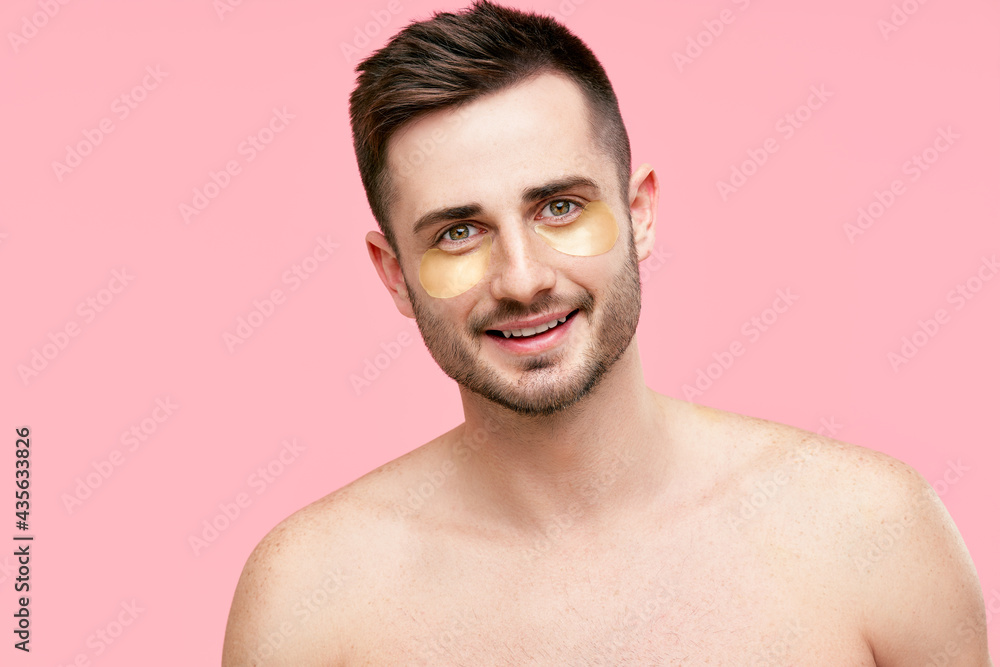 Naklejka premium Portrait of smiling handsome man with golden eye patches on pink background