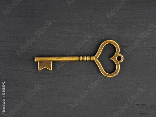 Bronze antique key with heart shaped hole on black wooden background