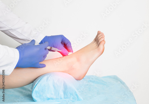 The doctor gives an intra-articular injection of an ankle block to a patient who has a ligament rupture and injury, close-up photo