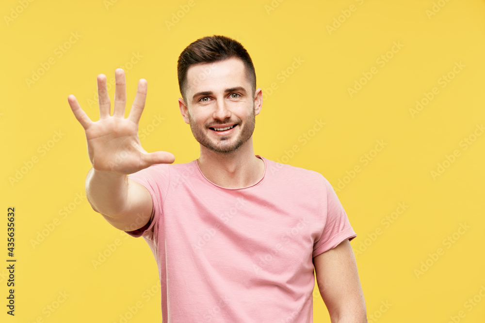 Portrait of smiling man with hand raised in greeting over yellow background Portrait of smiling man with hand raised in greeting over yellow background