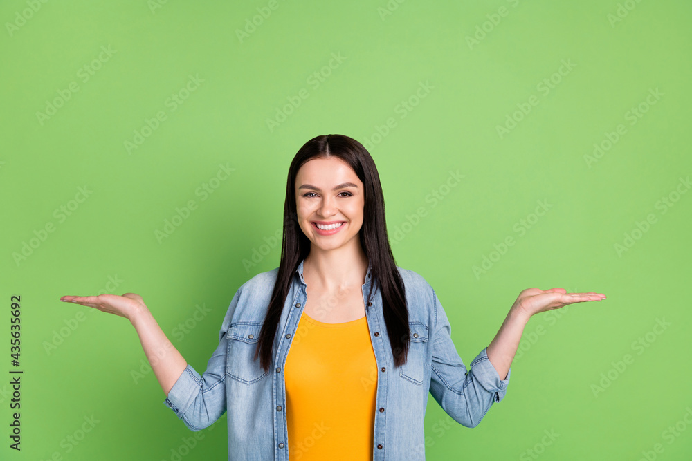 Photo of positive nice brown long hairdo lady hold hands empty space wear jeans shirt isolated on pastel green color background Photo of positive nice brown long hairdo lady hold hands empty space wear jeans shirt isolated on pastel green color background