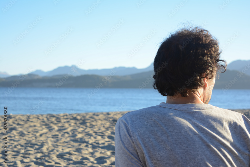 young male from behind on the beach looking at the lake young male from behind on the beach looking at the lake