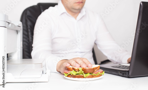 Male office worker in a white shirt with a sandwich in his hand. Workplace snack  breakfast