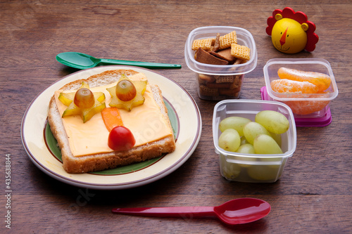 School lunch box snacks for kids over wooden background. Back to school. Healthy and fun snack option for moms. Cute food art creative concepts. Bow with fruits and vegetables and cute sandwich.