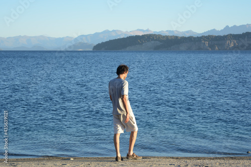 young male walking on the beach, with lake and mountains © Lautaro