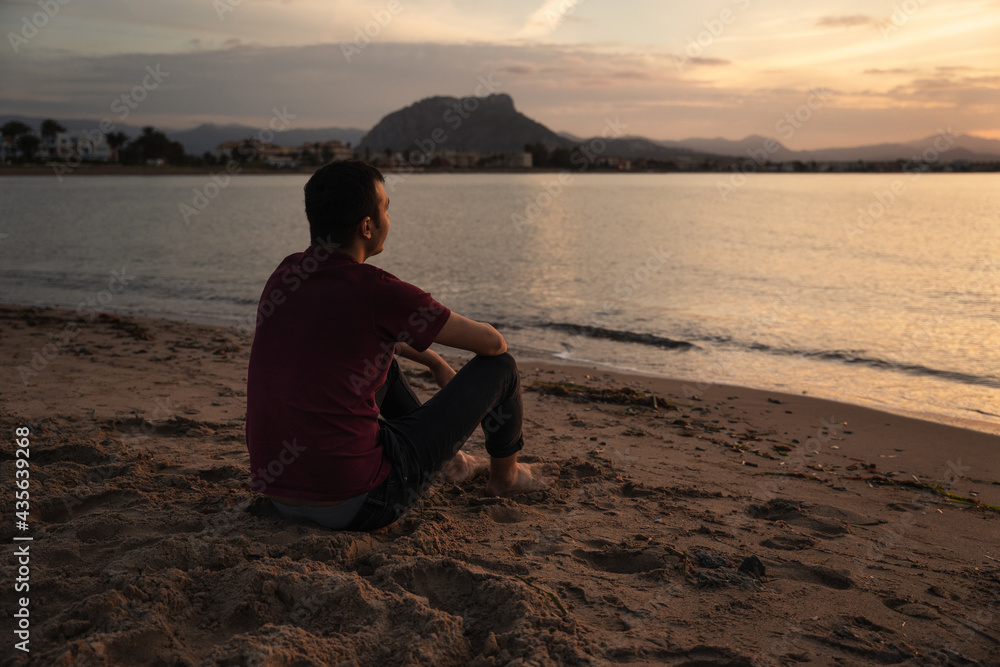 Man sitting on the seashore watching the sunset. He is sitting on the sand. The sea is calm. Mediterranean, Denia